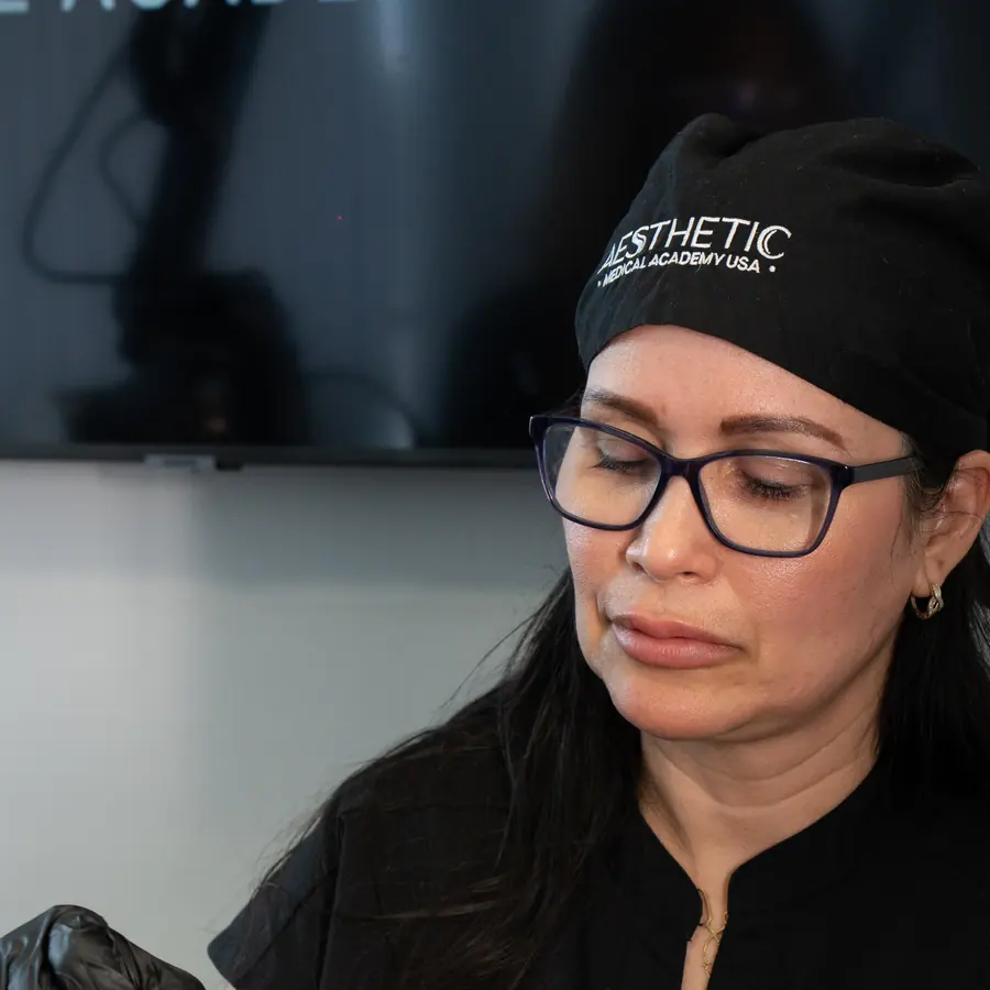 Instructora con gorro con el logo, mirando su trabajo en una clase de medicina estética