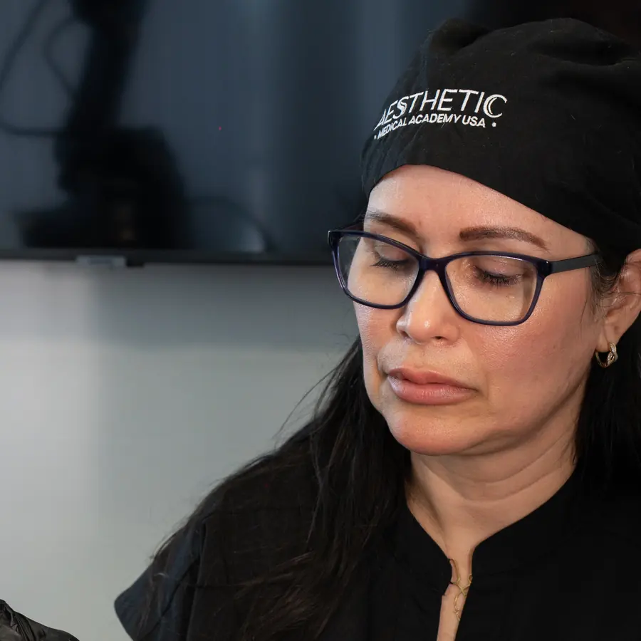 Instructora con gorro con el logo de la academia, concentrada durante una clase de inyectables