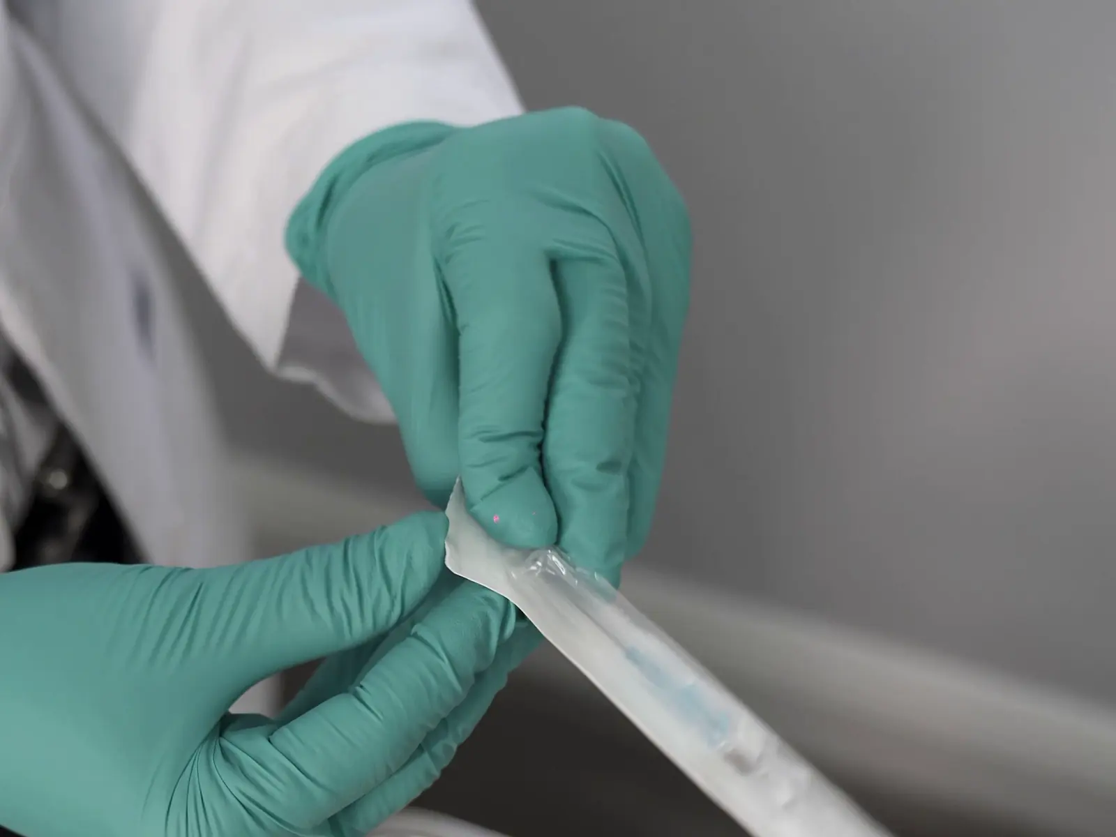 Manos con guantes abriendo una jeringa